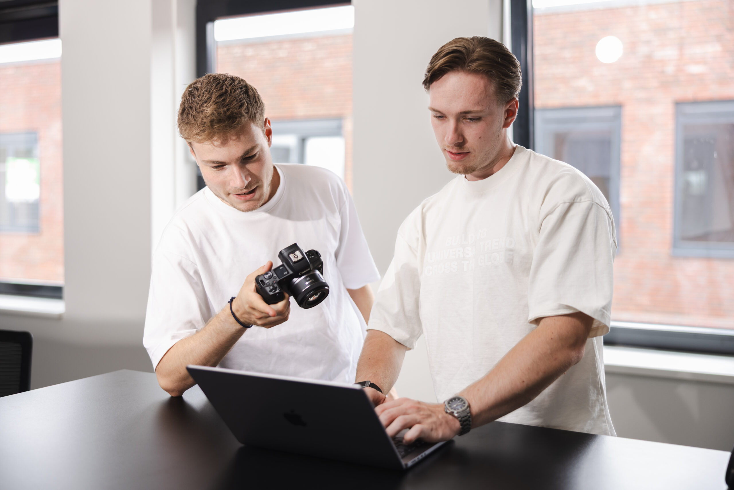 2 collega's staan achter een laptop met een camera in hun handen